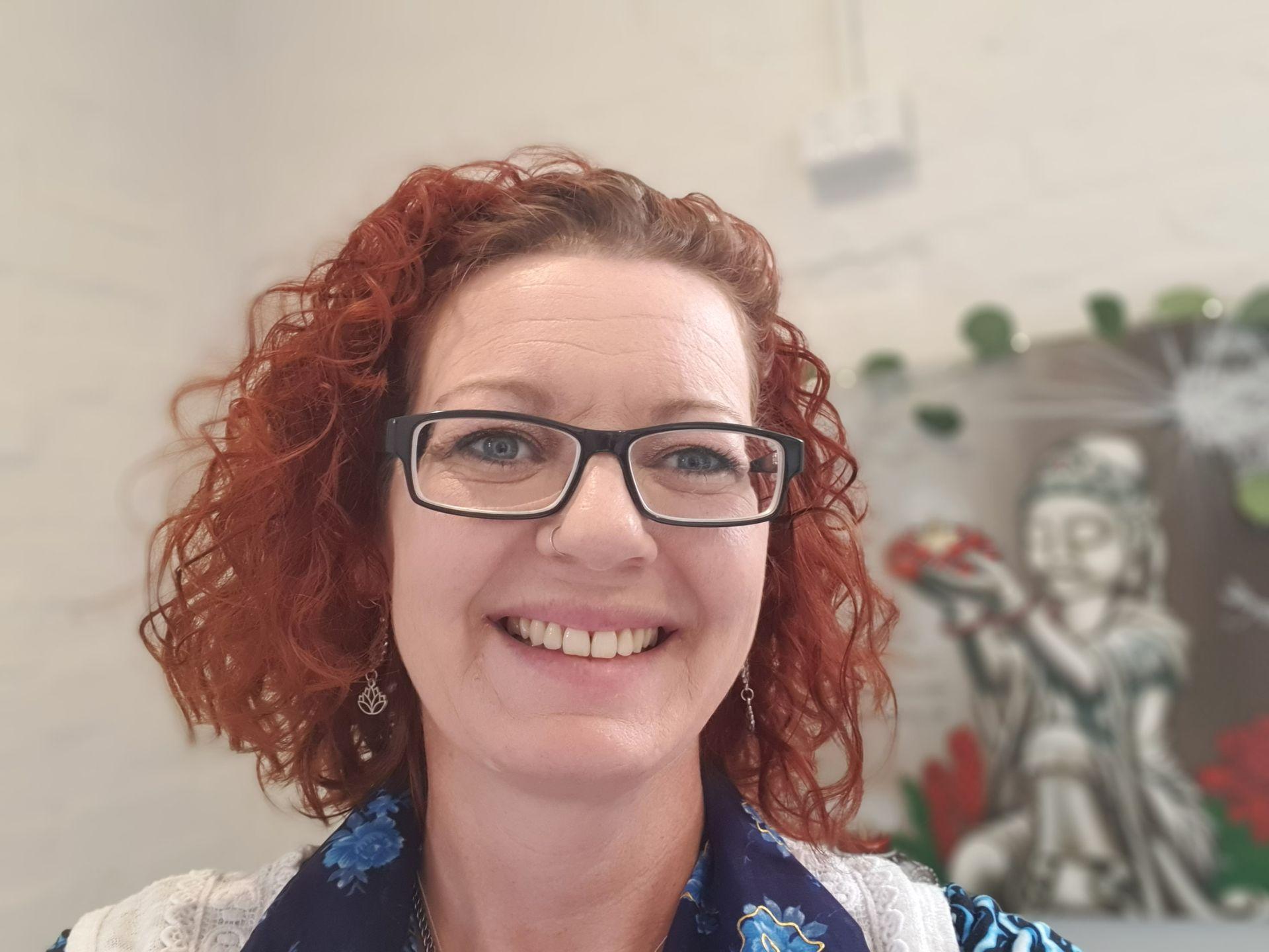 Smiling Lady with glasses, background picture of a painting of a peaceful Buddha