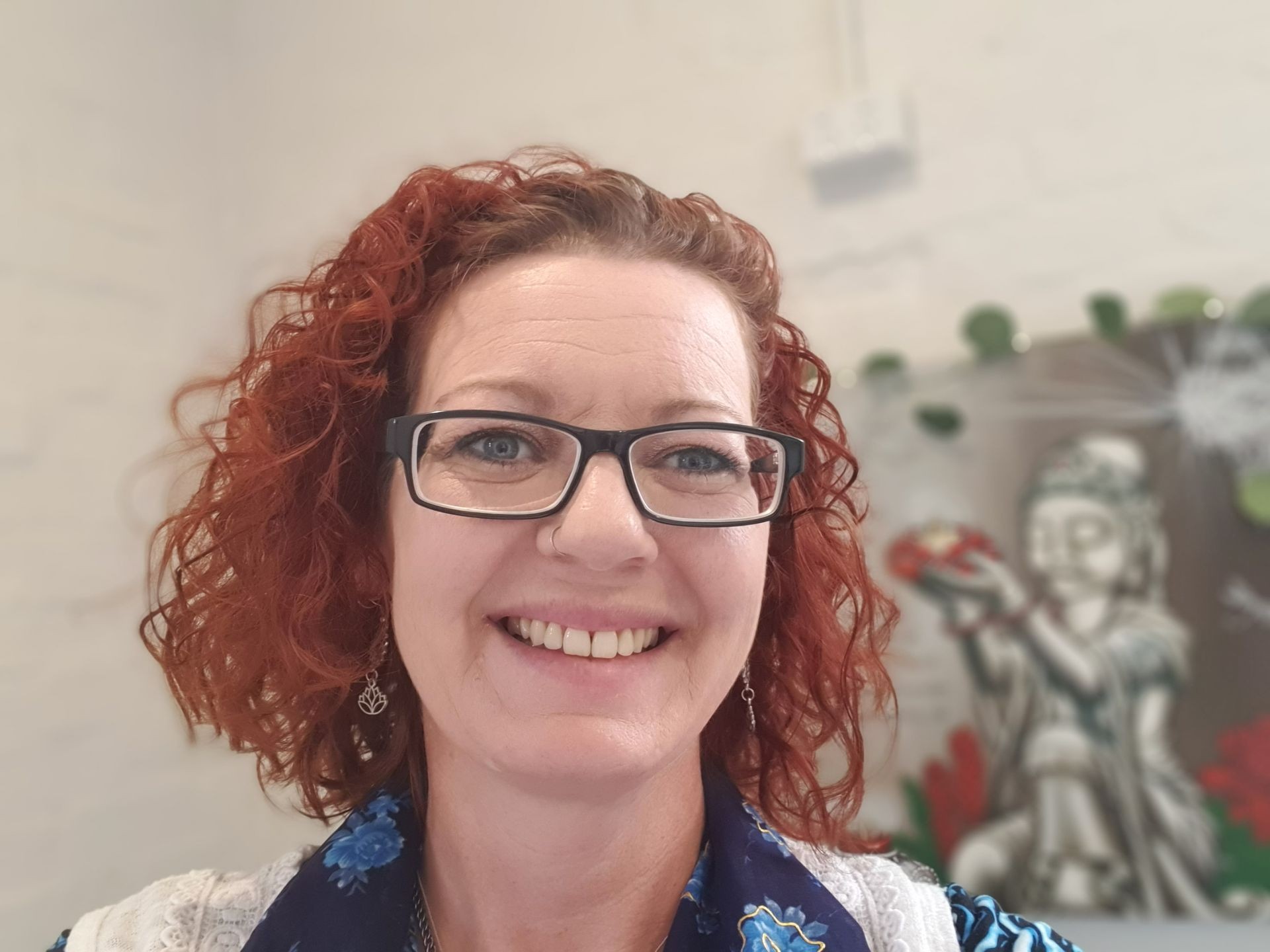 Reiki Master Teacher,  Smiling Lady, glasses, calming demeanour, curly bobbed auburn red hair. 