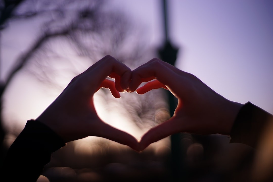 Silhouette of hands forming a heart shape against a purple sky at sunset.